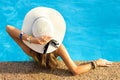 Back view of young woman with long hair wearing yellow straw hat relaxing in warm summer swimming pool with blue water on a sunny Royalty Free Stock Photo