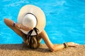 Back view of young woman with long hair wearing yellow straw hat relaxing in warm summer swimming pool with blue water on a sunny Royalty Free Stock Photo