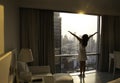 Back view of young woman looking at dawn city scenery and stretch the muscles at window. Health concept