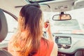 Back view young woman looking in rear view mirror and putting make up in car. Modern busy life. beautiful girl sitting in drivers Royalty Free Stock Photo