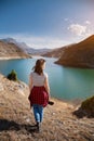 Back view young woman photographer with a photo camera in her hand stands on the shore of a high mountain lake on a Royalty Free Stock Photo