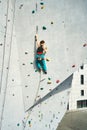 Back view young woman rock climber in bright blue pants climbing on vertical artificial rock wall Royalty Free Stock Photo