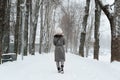 Back view of young woman in snow-covered coat and knitted white hat walking in park in winter, outdoors. Royalty Free Stock Photo