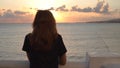 Back view of young woman standing on background of seascape at sunset. Media. Attractive woman stands on embankment on