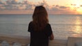 Back view of young woman standing on background of seascape at sunset. Media. Attractive woman stands on embankment on