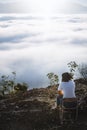 Back view of young woman traveler enjoying sunrise scenery view of fluffy sea fog misty clouds in high mountains Royalty Free Stock Photo