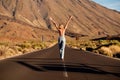 Back view of young woman walking along empty asphalt road in the middle of volcanic area with raised hands, topless. Freedom, Royalty Free Stock Photo