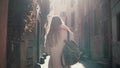 Back view of young woman walking at city street in Europe at morning. Girl exploring the old town alone, looking around. Royalty Free Stock Photo