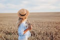 Back view of young woman walking in summer field wearing straw hat and linen shirt holding wheat bundle. Royalty Free Stock Photo