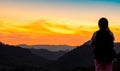 Back view of young woman watching beautiful sunset over mountain layer. Backpacker happy in travelling alone. Silhouette