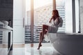 Back view of young woman wearing white bathrobe standing in bathroom looking out the window with bathtub in foreground Royalty Free Stock Photo