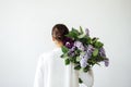 Back view of a young woman in a white shirt holding a bouquet of lilacs on her shoulder