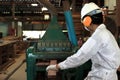 Back view of young wood worker in white safety uniform working with planing machine in factory.