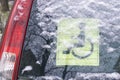 Back window of a car with the Disabled driving yellow sign. Covered with wet snow and water drops. The information sign says the c