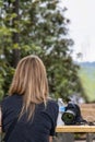 Back of woman with beautiful long streaked hair sitting at outside picnic table with camera and bottle of water beside her with bo