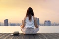 Back of woman relaxingly practicing meditation at the swimming pool rooftop with the view of urban skyline building to attain