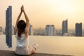 Back of woman relaxingly practicing yoga meditation at the swimming pool rooftop with view of urban skyline building to attain