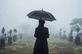 Back of woman wear all in black with umbrella on cemetery at rain foggy day. Grieving widow. Generative AI