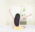 Back of young asian woman wearing yellow undershirt exercising yoga while sitting on a white bed by the window with a thin curtain Royalty Free Stock Photo