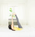 Back of young asian woman wearing yellow undershirt exercising yoga while sitting on a white bed by the window with a thin curtain Royalty Free Stock Photo