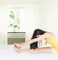 Back of young asian woman wearing yellow undershirt exercising yoga while sitting on a white bed by the window with a thin curtain Royalty Free Stock Photo