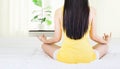 Back of young asian woman wearing yellow undershirt exercising yoga while sitting on a white bed by the window with a thin curtain Royalty Free Stock Photo