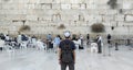 Back of a young tourist in casual clothes and kippah on the head looking at the wailing wall and religious praying near the sacred