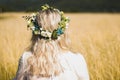 Back of the young woman in a white dress in boho style with a floral wreath in the summer in the field