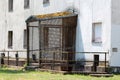 Backdoor entrance to large old industrial building protected with wire mesh and moss covered roof surrounded with rusted fence