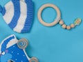The background is baby blue. With a wooden rattle, a blue wooden elephant and a knitted cap for babies in blue and white