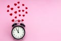 Black alarm clock and red hearts around it on a pink background. Place for text. Valentine`s Day. Time for love