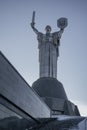 on the background of the blue sky stands a large monument Motherland Motherland with a new trident on the shield