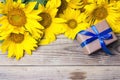 Background with a bouquet of yellow sunflowers and gift box with blue ribbons on a wooden table. Royalty Free Stock Photo