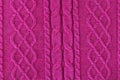 Background from a fabric texture. Wool knitted fabric with cable seamless pattern of pink-red color. Textile closeup