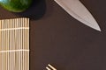 Background flat lay of a sushi making table. Makisu bamboo board, chopsticks, avocado and a knife on black background Royalty Free Stock Photo