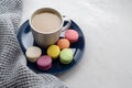 Background with gray plaid, coffee with milk, cappuccino and multi-colored appetizing macaroons, top view, copy space