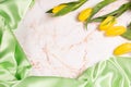 Background with green silk fabric on light marble and yellow tulips Royalty Free Stock Photo