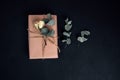 Background for greetings. Gift wrapping in soft pink paper with dry eucalyptus branch on a black concrete background Royalty Free Stock Photo