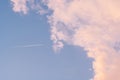 Background image of blue bright sky with pastel pink and white clouds and airplane with trail. Royalty Free Stock Photo
