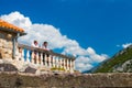 Background image. In the background is a blurred landscape of tourists, an old building, mountains and a blue sky