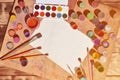 Background image showing interest in watercolor painting and art. A blank sheet of paper, surrounded by brushes, cans with waterc