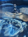 Background image of water droplets falling on water in a blue container and splashing up. Royalty Free Stock Photo