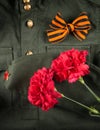 On the background of military clothing, two red carnations and St. George ribbon in the form of a bow Royalty Free Stock Photo