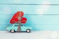 Background with miniature blue toy car carrying a heart on blue