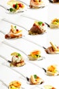 Background of mixed canapes on metal spoons. White background