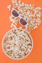 Background. Popcorn, cup and 3d glasses on a colored orange background. Flat lay Royalty Free Stock Photo