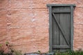 Background of red brick wall with wooden plank door and growing grass, copy space for text Royalty Free Stock Photo