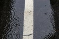 Background of rippled water pooled on a black asphalt parking lot with white parking stripes during a rain