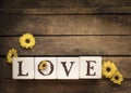 Blocks of wood that spell LOVE with a scattering of yellow daisy on rough wood with room for text
