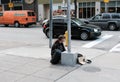 Homeless man seen sitting by the side of a road crossing in a busy city.